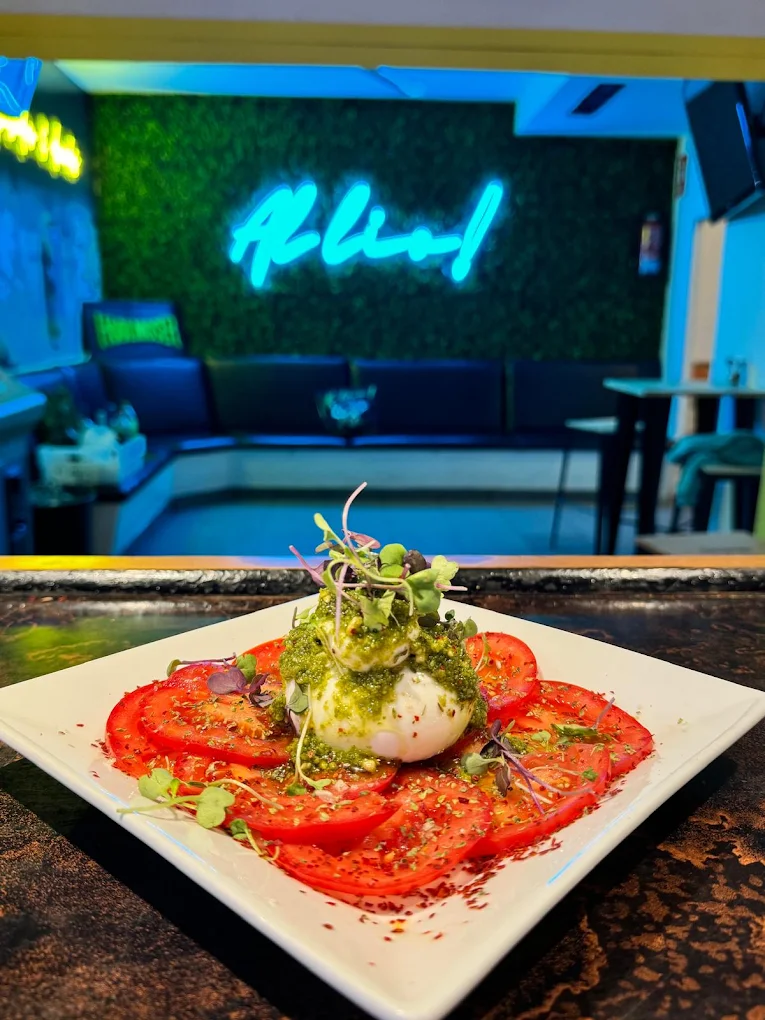 Burrata con tomate, pesto y brotes frente al neón de AL LÍO!